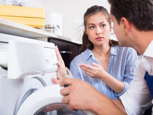 Frau und Mechaniker vor kaputter Waschmaschine