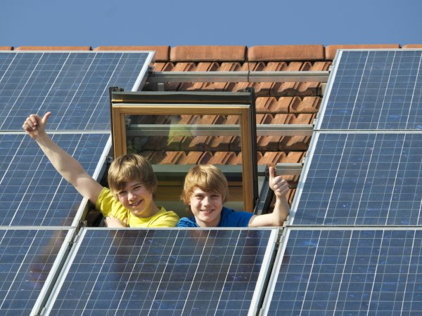 Kinder im Dachfenster freuen sich über Solarzellen auf ihrem Haus