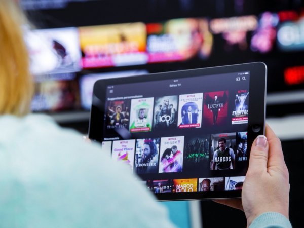 Person sitzt vor Tablet und vor Fernseher 