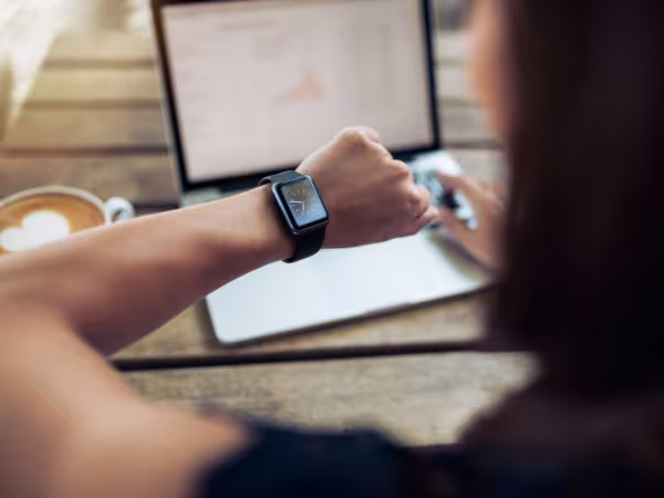 Frau schaut vor Laptop auf Uhr