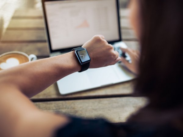Frau schaut vor Laptop auf Uhr