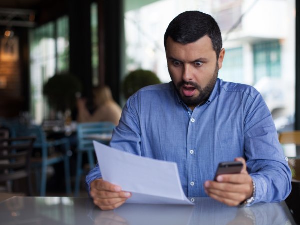 Verbraucher mit Smartphone in der Hand schaut erschrocken auf Telefonrechnung