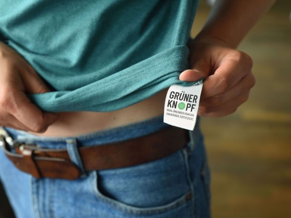 Textsiegel Grüner Knopf an einem petrolfarbenem T-Shirt