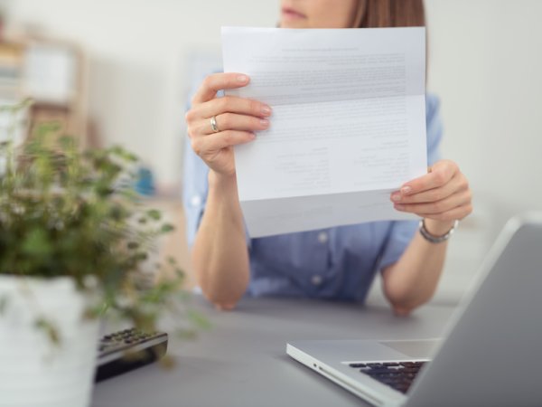 Eine Person sitzt an einem Tisch vor einem Laptop und hält einen Brief hoch.