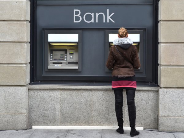 Junge Frau holt bei einer Bank Geld am Geldautomaten